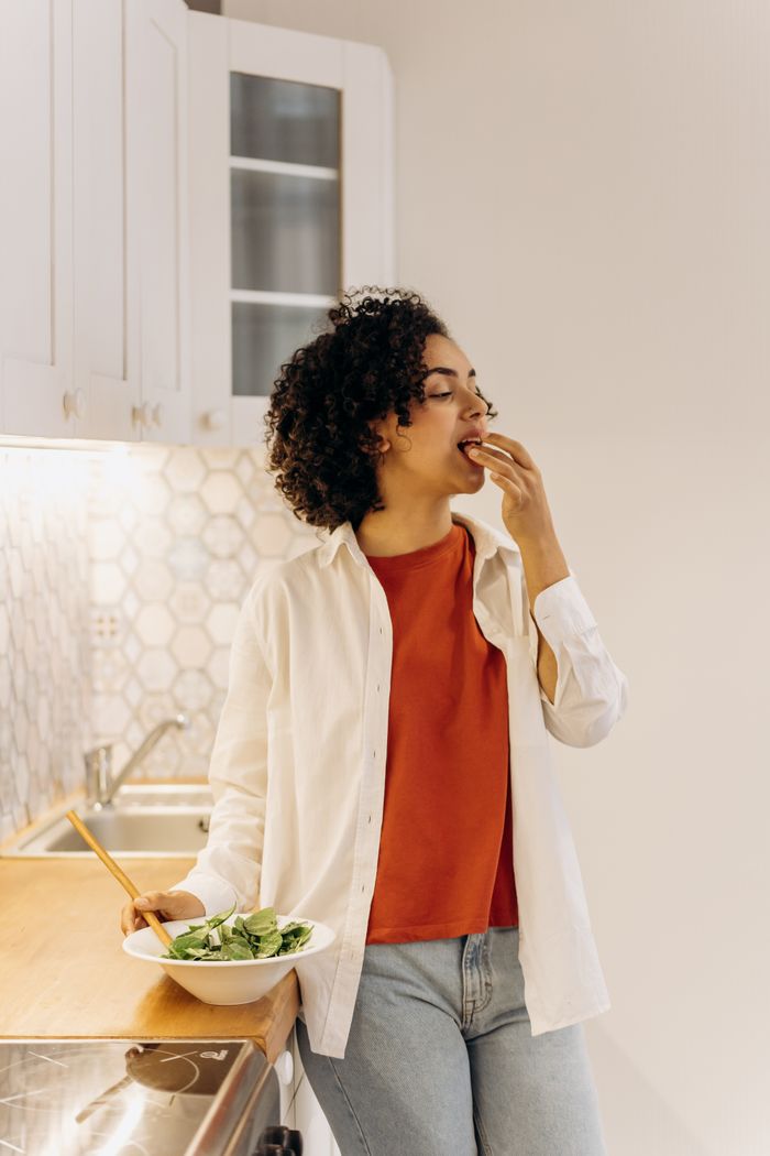 Young woman eats a fresh salad in a bright, modern kitchen, embracing a healthy lifestyle.